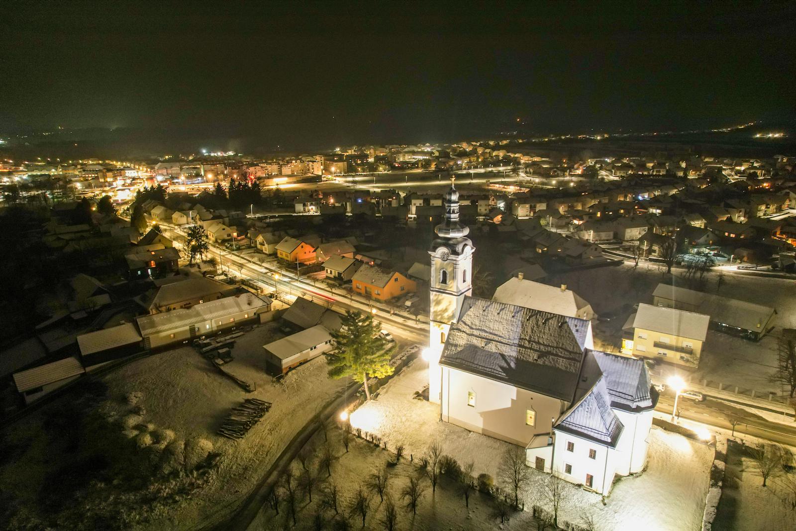 Aerial drone shot capturing a snow-covered town and illuminated church at night, showcasing winter scenery.